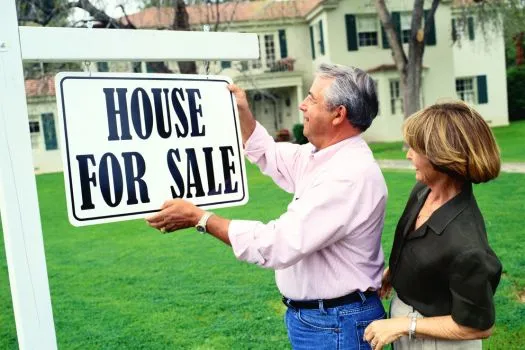 A couple hanging a "For Sale" sign in the front yard.